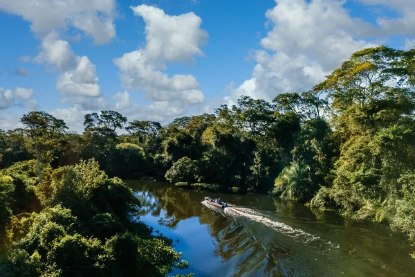 Uma lancha no lago cercada por belas árvores verdes sob um céu nublado. Metrópoles