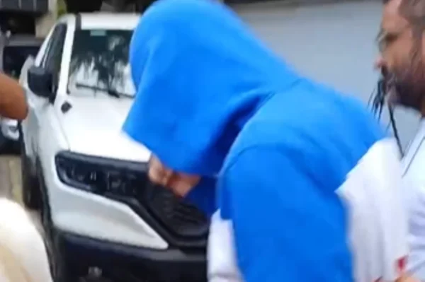 Imagens coloridas mostram homem com blusa azul e branca, capuz azul, escoltado por policial