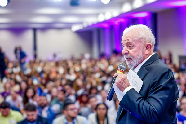 Imagem colorida de presidente Lula segurando um microfone, de lado, em meio a uma multidão desfocada - Metrópoles