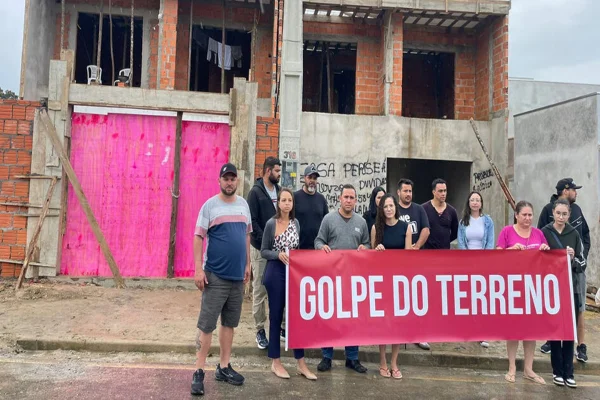 Imagem colorida, pessoas segurando uma faixa em frente a um terreno - Metrópoles