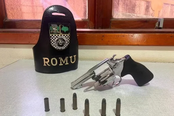 Imagem colorida de arma posta sob uma mesa. Metrópoles