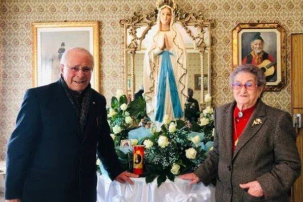 Um casal de idosos posa junto a uma imagem de Nossa Senhora