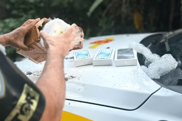 Imagem colorida de um policial averiguando celulares escondidos por motoboy - Metrópoles