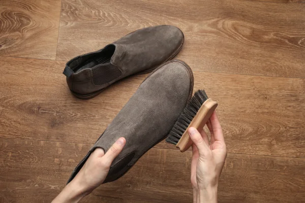 Mãos limpando sapatos de camurça com uma escova no chão. Vista superior. Cuidados com os sapatos