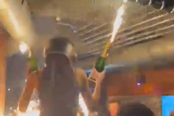 Foto colorida de mulher segurando velas pirotécnicas próximo a teto de bar na Suíça - Metrópoles