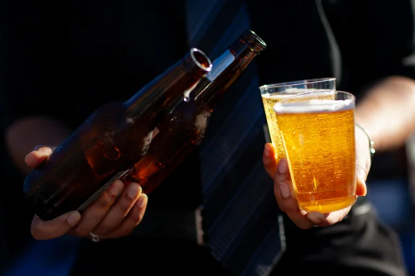 Foto colorida de homem segurando garrafas e copos de cerveja - Metrópoles