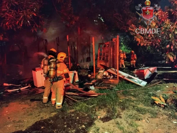Foto colorida tirada à noite de quatro bombeiros em meios à escombros carbonizados