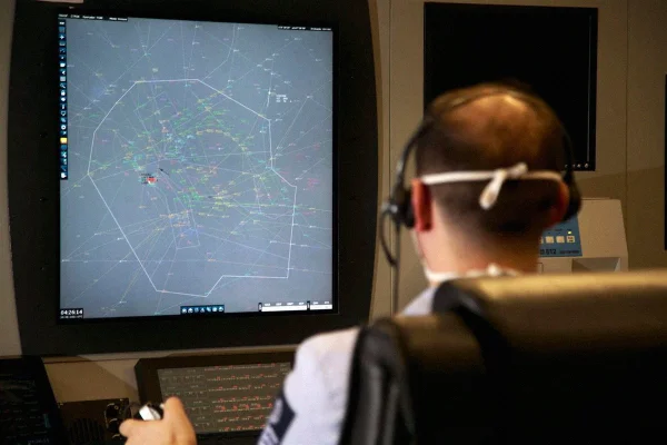 Homem de costas trabalha diante de um computador de controle aéreo