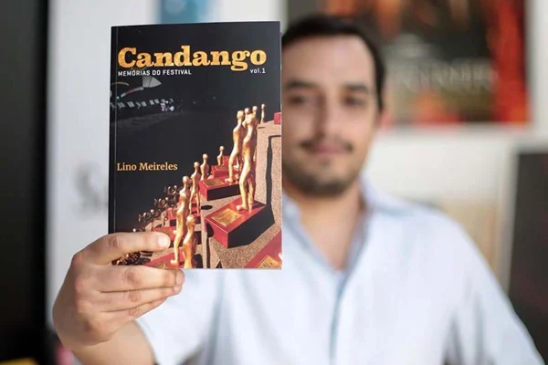 Foto colorida de Lino Meireles segurando livro - Metrópoles
