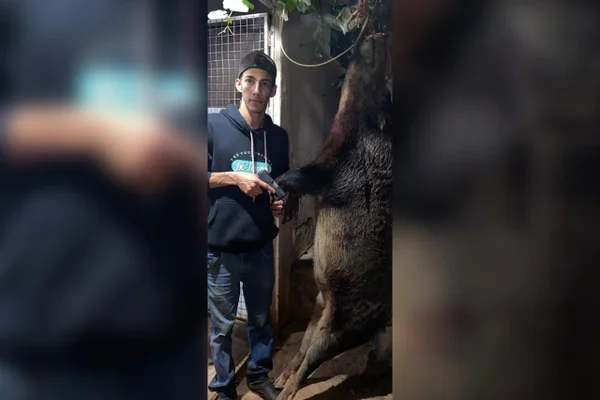Imagem colorida de um homem segurando uma arma de fogo ao lado de um animal morto -Metrópoles