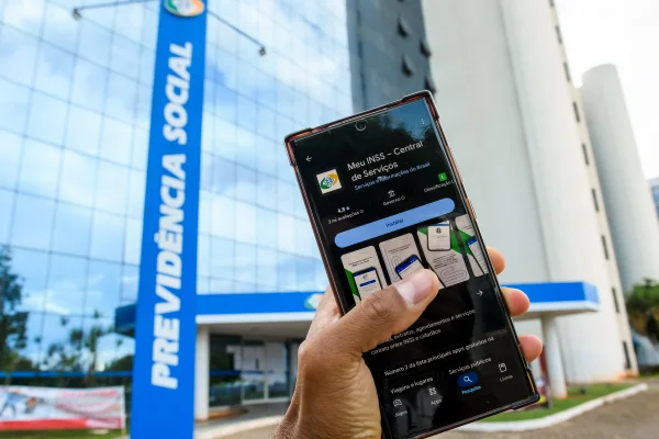 Fachada da Previdência Social e acesso digital aos serviços do INSS pelo aplicativo Meu INSS - Mertrópoles