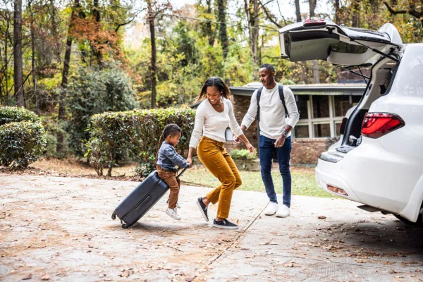 Foto colorida de família com malas em direção ao carro