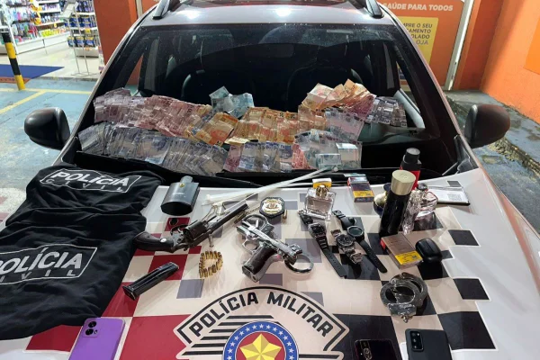 Imagem colorida mostra armas e dinheiro em cima de carro da PM - Metrópoles