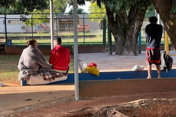 Pessoas agasalhadas, de costas, sentadas em banco no parque