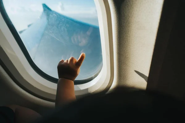 Mão cortada de uma criança apontando a janela do avião contra o céu azul enquanto viaja - Metrópoles