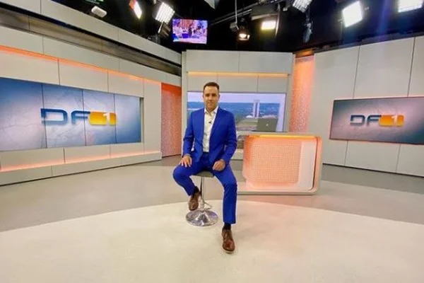 Fotografia colorida de homem de terno sentado em cadeira de estúdio de TV