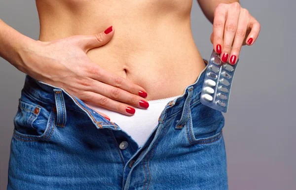 Mulher sem camisa com uma das mãos na barriga enquanto a outra segura remédios- Metrópoles