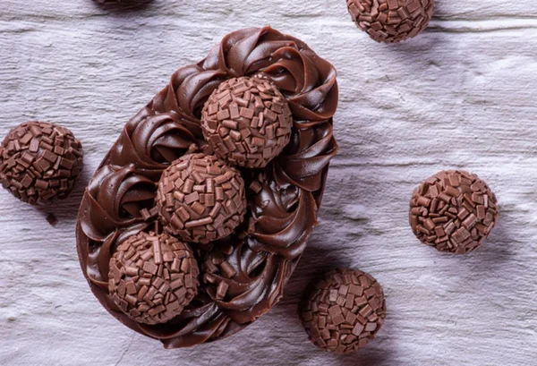 Ovo de pascoa de colher sabor brigadeiro em cima de uma bancada cinca com vários brigadeiros em volta - Metrópoles