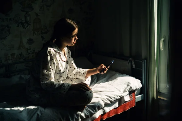 Retrato de uma adolescente com celular sentada à janela de uma casa na aldeia. Conceito de depressão, solidão, problemas da adolescência. Metrópoles