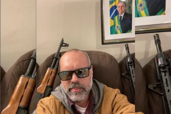 Allan dos Santos posa com fuzis e foto de Bolsonaro