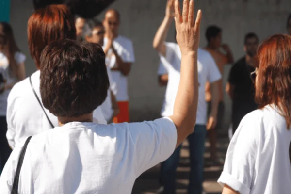 Imagem colorida de pessoas com as mãos para cima em um evento voluntário - Metrópoles
