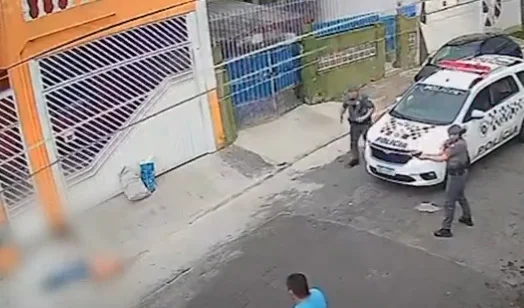 Imagem de policiais ao lado de viatura apontando armas para homem caído na rua - Metrópoles