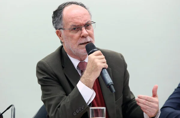 Imagem colorida mostra Barjas Negri, homem branco, calvo, grisalho, de barbas brancas, de terno marrom e gravata vermelha, falando ao microfone em uma mesa - Metrópoles