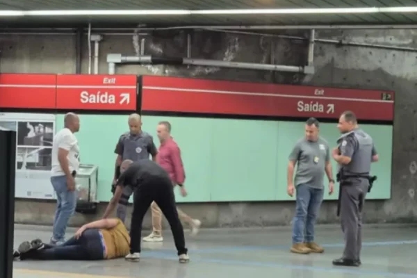 Imagem colorida de homem baleado caído no chão e policiais à sua volta. Metrópoles
