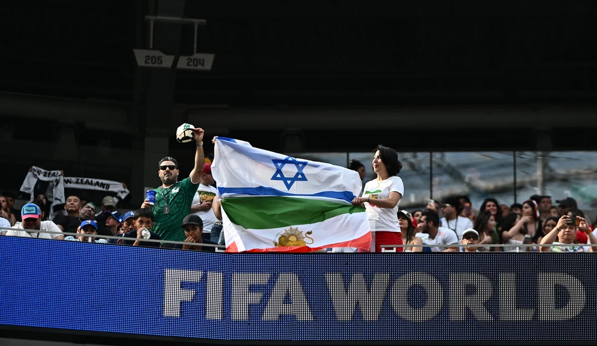 Torcedores do Irã posam para uma foto com uma bandeira iraniana pré-revolucionária unida a uma bandeira de Israel durante a partida do Grupo G da Copa do Mundo da FIFA 2026 entre Irã e Nova Zelândia no Estádio de Los Angeles Torcedores do Irã posam para uma foto com uma bandeira iraniana pré-revolucionária unida a uma bandeira de Israel durante a partida do Grupo G da Copa do Mundo da FIFA 2026 entre Irã e Nova Zelândia no Estádio de Los Angeles
