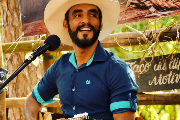 homem de barba e chapeu de caubói canta sentado com violao