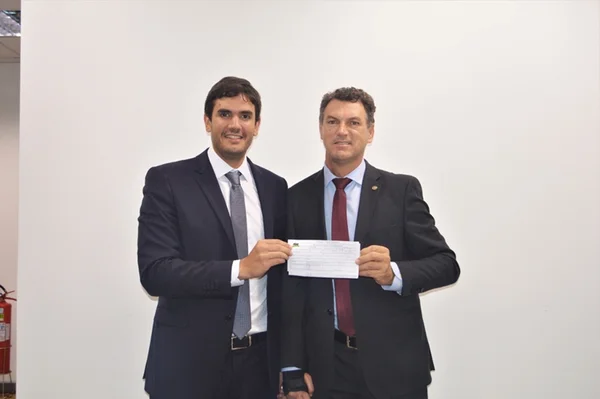Dois homens de terno e gravata segurando papel e sorrindo