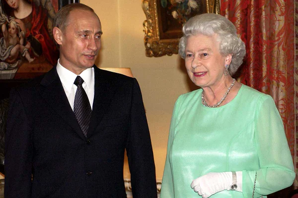 Vladimir Putin, de terno, e a Rainha Elizabeth, de vestido verde, lado a lado em ambiente interno. Ambos sorriem - Metrópoles