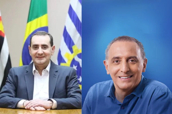 Imagem colorida mostra um homem branco, de terno, sentado com bandeiras atrás. Ao lado, outro homem branco, camisa azul e fundo também azul