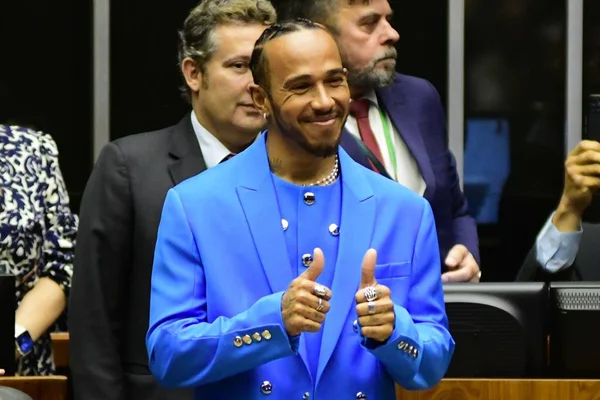 O piloto britânico Lewis Hamilton na Câmara dos Deputados para receber título de cidadão honorário do Brasil. Na foto, ele sorri e faz sinal de joia com as mãos no plenário da casa legislativa - Metrópoles