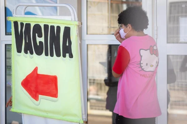 Placa escrito vacina com seta vermelha e menina com camisa rosa da Hello Kitty ao lado