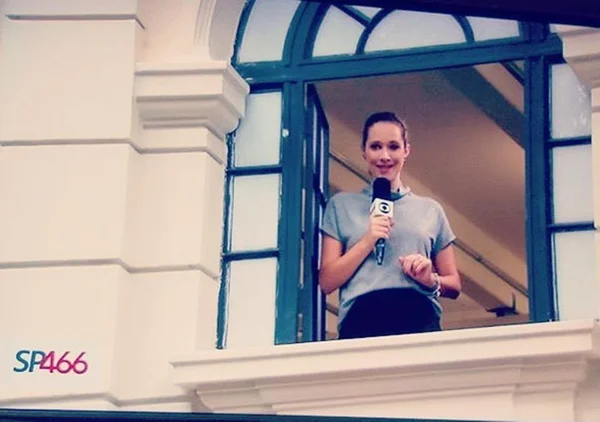 Natália Ariede na sacada de prédio com microfone na mão