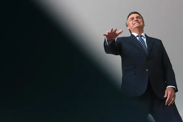 Após encontro com prefeito, BoApós encontro com prefeito, Bolsonaro fala com a imprensa no Palácio do Planalto. Na foto, ele sorri e ergue a mão - Metrópoles