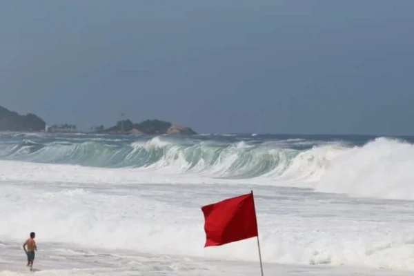 foto colorida de ondas em praia, com bandeira vermelha de alerta - Metrópoles