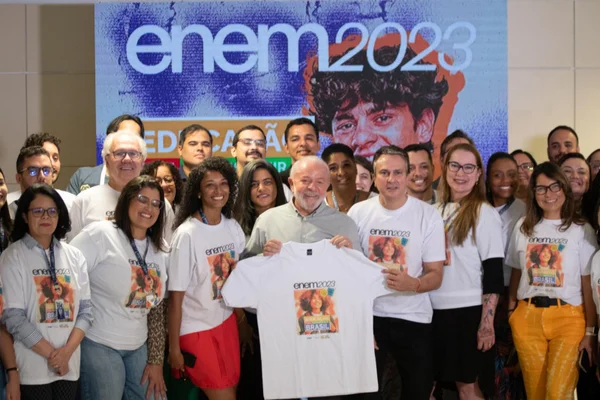Imagem colorida mostra o presidente Lula segurando uma camiseta branca cercado por várias pessoas que também vestem uma camiseta branca na sede do Inep - Metrópoles