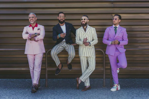 Homens com ternos coloridos encostados em uma parede marrom clara