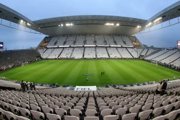 Imagem do estádio do Corinthians mostra visão desde as cadeiras centrais, com o gramado e as cadeiras vazias