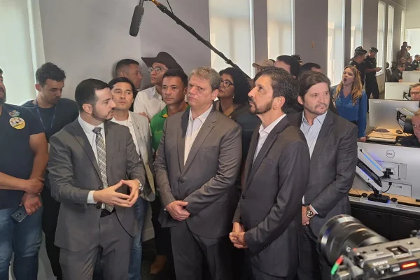 Imagem colorida mostra grupo de homens de terno em uma sala de monitoramento