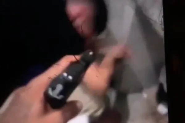 Imagem colorida de mão apontando pistola em direção a rapaz, sentado no chão, com a cabeça baixa - Metrópoles