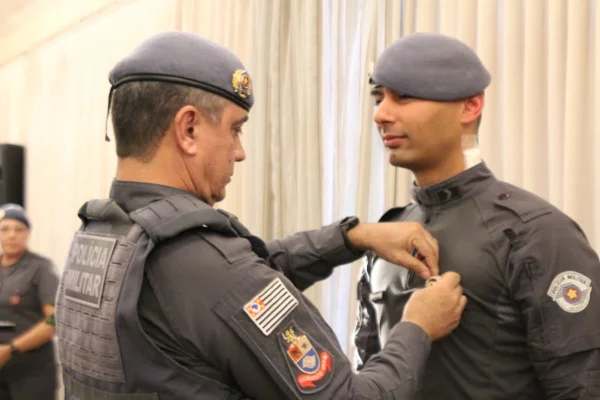 Policial militar fardado com uniforme cinza escuro coloca medalha em outro, vestido da mesma forma - Metrópoles
