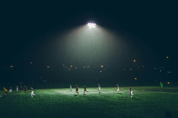 Imagem mostra campo de futebol amador iluminado com jogadores - Metrópoles