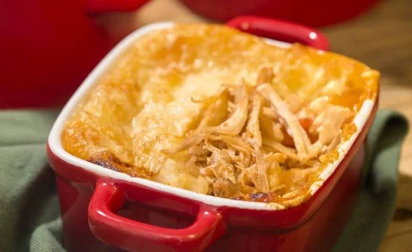 Na foto temos uma panelinha vermelha por fora e branca por dentro com escondidinho de pernil