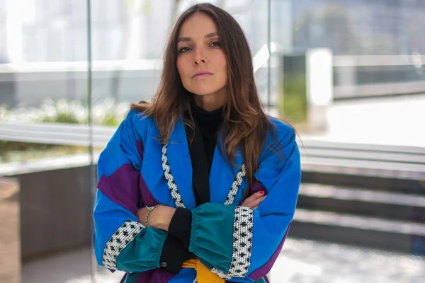 Yasmine McDougall Sterea, ex-editora da Revista Vogue Brasil e fundadora do projeto Free Free. Ela é uma mulher jovem e branca, de cabelo longo liso e castanho, posando para foto no terraço de um prédio. Usa uma blusa preta de gola aula e um casaco colorido por cima.