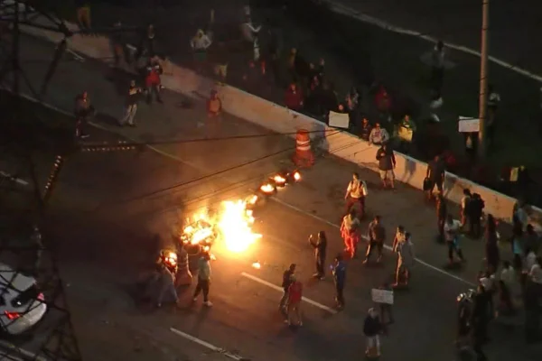Imagem colorida feita do alto mostra um grupo de pessoas no meio de uma pista de carros. Elas estão em torno de uma fogueira formada por pneus queimados - Metrópoles
