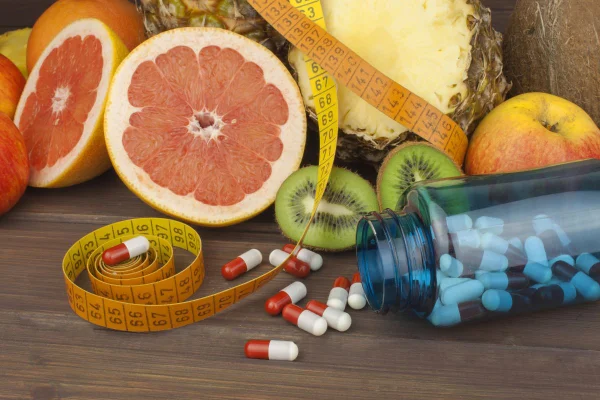 frutas, suplementos em cápsula e uma fita métrica