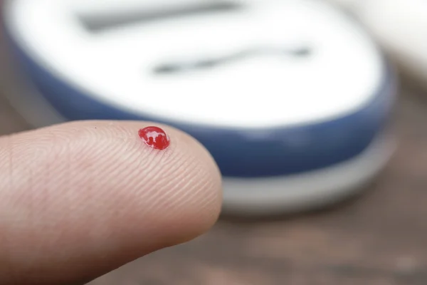 Foto colorida de dedo com gota de sangue e um tipo de dospositivo medidor de glicose ao fundo - Metrópoles.